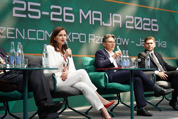Prezes PolKa podczas panelu dyskusyjnego na konferencji, siedząca na scenie z mikrofonem, wśród innych panelistów na tle zielonej scenografii wydarzenia.